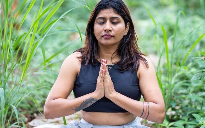 Person meditating outdoors surrounded by greenery