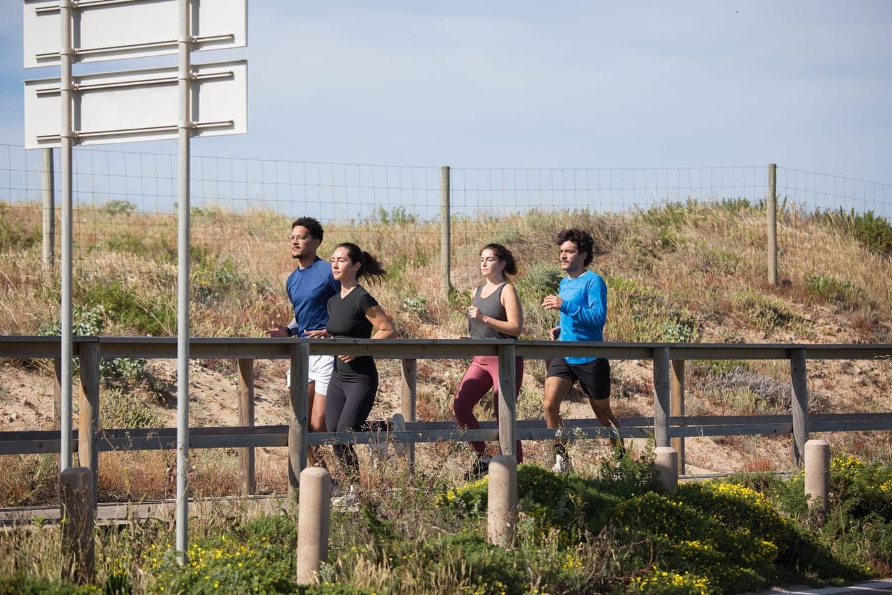 Four people jogging together on a sunny coastal boardwalk